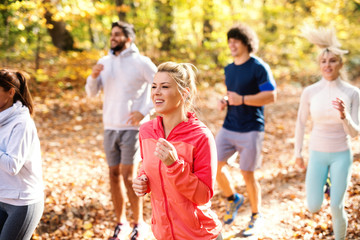 Fototapeta premium Small group of people running in woods in the autumn. Selective focus on blonde woman.