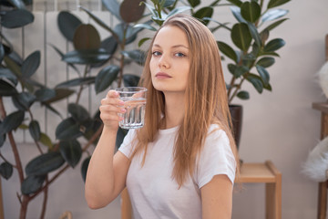 woman drinking water in the morning at home. detox concept, health care. blonde in a white T-shirt in a cozy room.