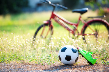 football and soccer shoes with blurry of red bicycle and green grass