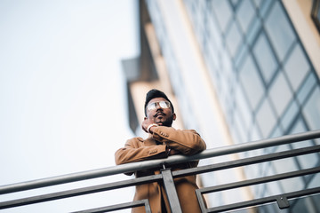 Young happy Indian businessman smiling with arms on handsrail at rooftop of business center