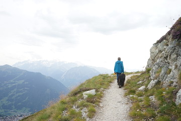 Fototapeta na wymiar Male hiker and a Bernese Mountain Dog walking on the path in the mountains, Alps, Switzerland