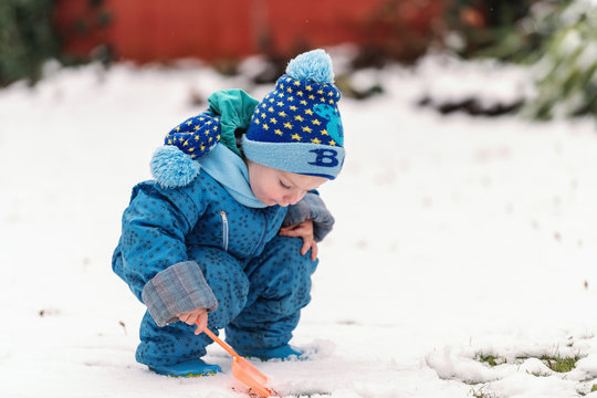 Cute Caucasian little boy in warm clothes and with scarf and hat playing on the snow with little shovel.