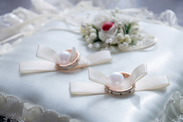 gold wedding rings on white silk cushion close up