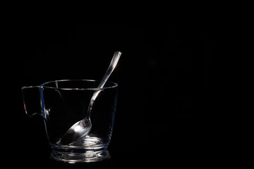 Glass mug with a teaspoon on a black background