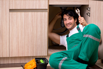 Young plumber repairing wash basin at kitchen  