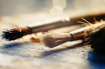 Several bristle brushes lie on a palette stained with blue and yellow oil
