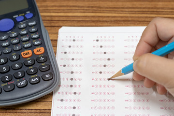 Dry hand of mature student doing exams by using pencil selected multiple choice on standardized test form with answers bubble with calculator nearby. Ideas about adult education and life long learning