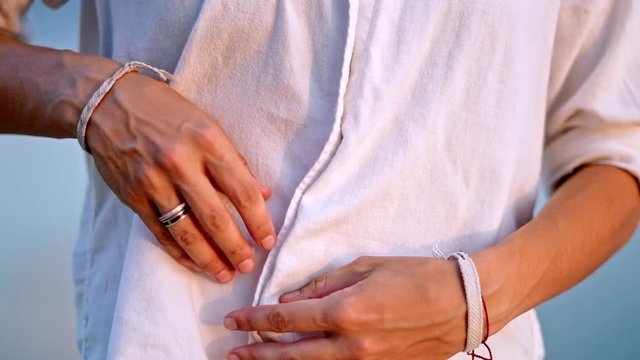 A young woman unbuckles a white shirt, exposing a tight belly.