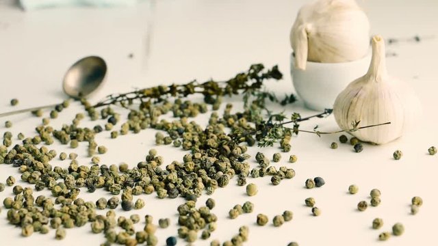 Green peppercorns - pepe verde - famous spice of italian cuisine on white table with garlic bulbs, thyme twig and spoon. Pouring green peppercorns on white table.