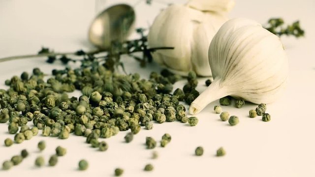 Green peppercorns - pepe verde - famous spice of italian cuisine on white table with garlic bulbs, thyme twig and spoon. Pouring green peppercorns on white table.