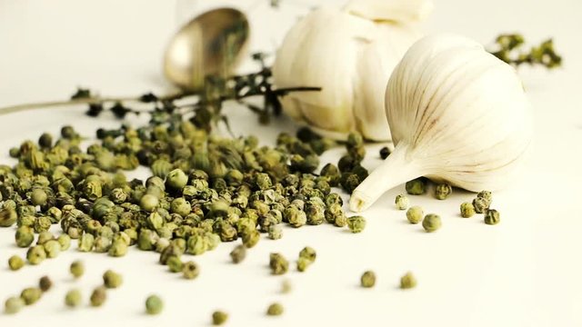 Green peppercorns - pepe verde - famous spice of italian cuisine on white table with garlic bulbs, thyme twig and spoon. Pouring green peppercorns on white table.