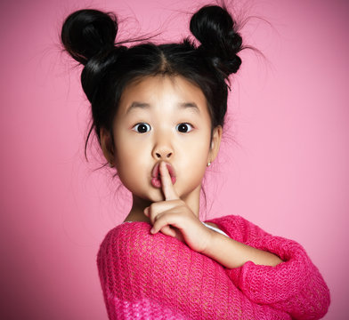 Asian kid girl in pink sweater shows shh sign Close up portrait