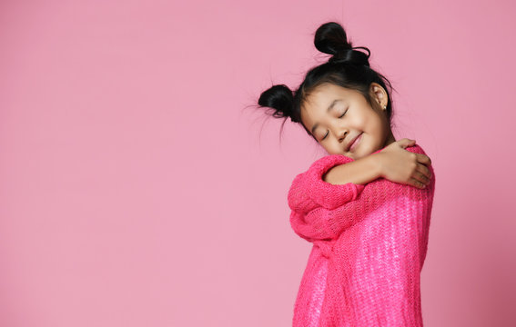 Asian kid girl with closed eyes in pink sweater hug herself and dream