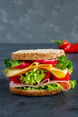 Graham bread sandwich with ham, cheese and fresh vegetables on a dark background. Breakfast concept.