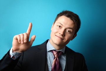 Young businessman in suit on blue background shows his hand thumbs up, symbol of success.