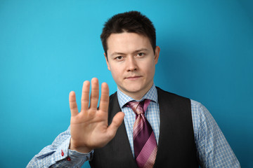 Young businessman in suit on blue background holds his hand in front of him, stop sign.