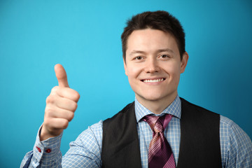 Young businessman in suit on blue background shows his hand thumbs up, symbol of success.