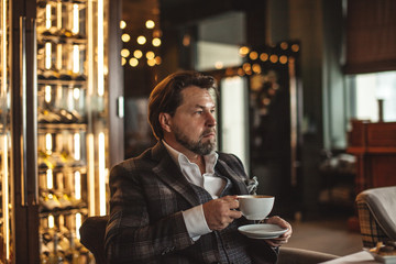 Confident thoughtful artist, wealthy man having a cup of tea, enjoying minutes of rest while waiting someone in the modern popular restaurant