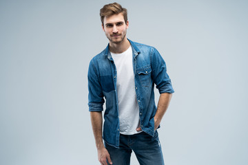 Portrait of stylish, stunning man in denim outfit standing over grey background.