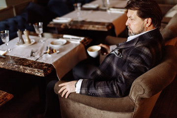 Confident thoughtful artist, wealthy man having a cup of tea, enjoying minutes of rest while waiting someone in the modern popular restaurant