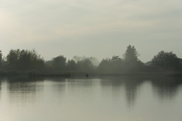 Obraz na płótnie Canvas Fog over calm lake, angler on the boat
