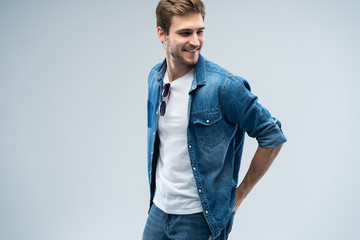 Portrait of stylish, stunning man in denim outfit standing over grey background.