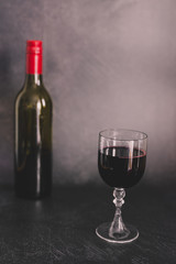 glass of intensely coloured red wine and bottle on dark background
