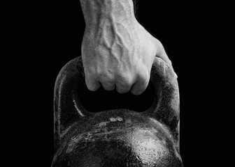 Kettlebell on a black background. The fist of an athlete clutching kettlebell. Close-up of a muscular hand holding a kettlebell