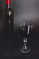 glass of intensely coloured red wine and bottle on dark background