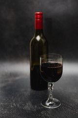 glass of intensely coloured red wine and bottle on dark background