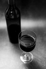 glass of intensely coloured red wine and bottle on dark background