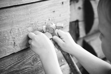 The child holds a hammer, hammer a nail into the old board
