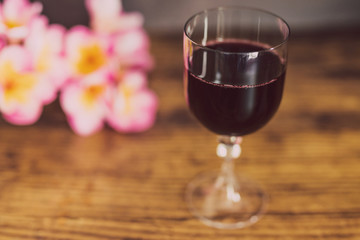 glass of intensely coloured red wine and tropical Australian flowers on wooden table
