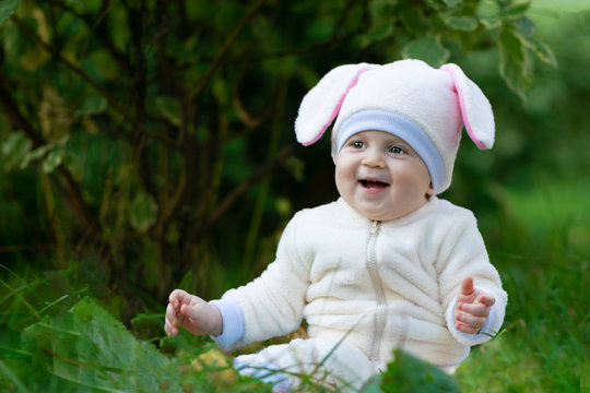 Chubby child in bunny suit seating on grass in park and laughing.