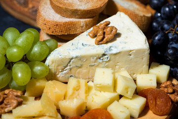 cheese platter on a wooden board, bread and fruit, closeup top view