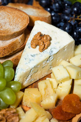 cheese platter on a wooden board, bread and fruit, closeup