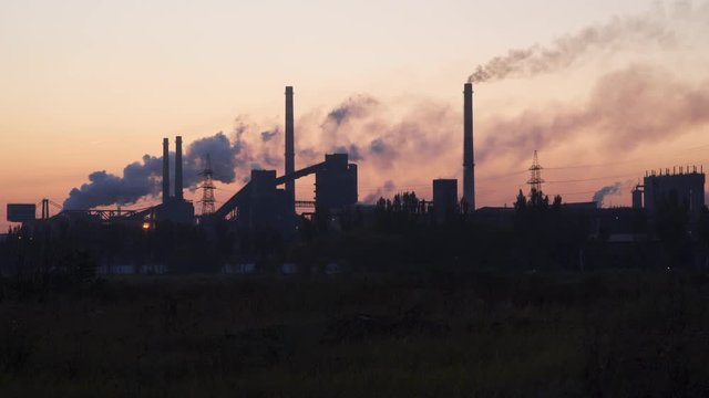 Silhouettes of buildings of the metallurgical plant against the sky at sunrise