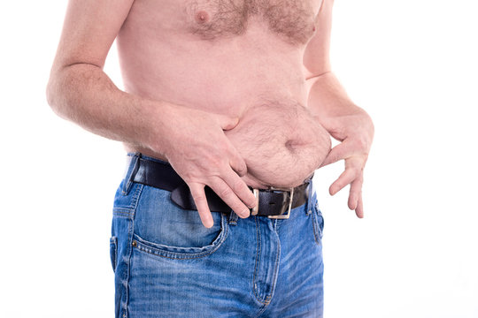 Young topless man touches his fat stomach with two hands islolated on white background - concept getting rid of belly fat, belly button, overweight, diet, lifestyle, health, ugly, weight loss or gain
