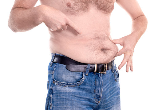 Young chubby man measures his fat stomach and points on it with finger islolated on white background - concept getting rid of belly fat, overweight, ugly, diet, lifestyle, health, weight loss or gain