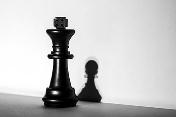 The chess king stands in the spotlight, which transforms the shadow of a pawn into an artistic...