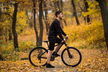 Fototapeta premium Handsome man biker in professional sportswear looking to side while riding bike down park alley on autumn day. Sportsman training thinking about future win in contest. 