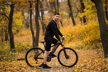 Obraz na płótnie Canvas Handsome young Mountain Bike cyclist is standing under the tree in the forest