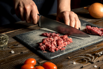 cook hands cut red meat on the board. nearby are tomatoes, onion, butter