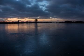 Naklejka premium Cloudy sky after sunset from the frozen lake and reflecting light on the ice