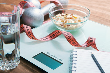 Healthy diet, fitness and weight loss concept. Scales, measuring tape, dumbbells, oatmeal, apple, a glass of water, an open notebook and a pencil on the table