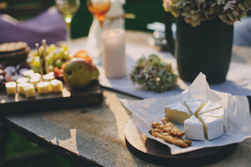 summer outdoor garden table setting with flowers, candles, white wine, cheese and fruits