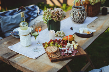 summer outdoor garden table setting with flowers, candles, white wine, cheese and fruits