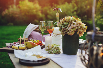 summer outdoor garden table setting with flowers, candles, white wine, cheese and fruits