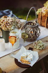 evening summer garden party with wine, cheese and fruits on wooden table decorated with candles and flowers