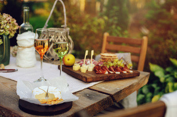 summer garden table decorated with flowers and candles, evening party with wine, cheese and fruits